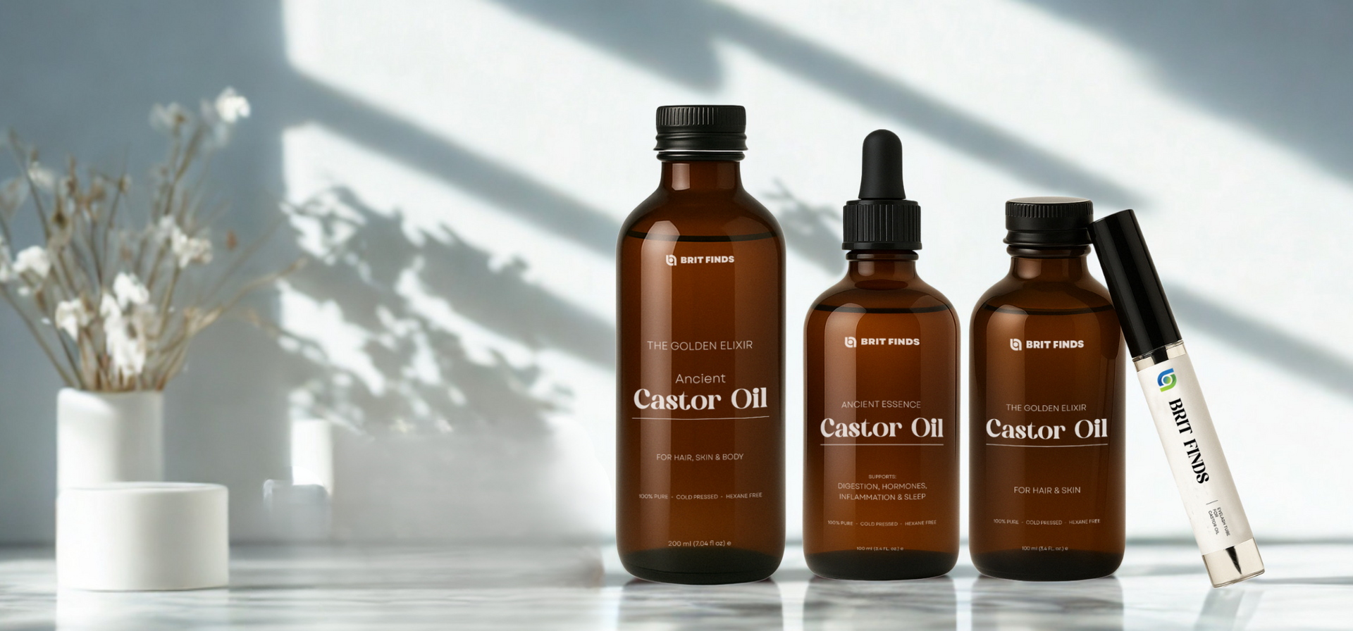 Brit Finds castor oil collection displayed on a clean marble surface with natural light – includes 100% pure, cold-pressed castor oil bottles for hair, skin, digestion, inflammation, and sleep, plus an eyelash tube with wand inside it – perfect for natural wellness and beauty.