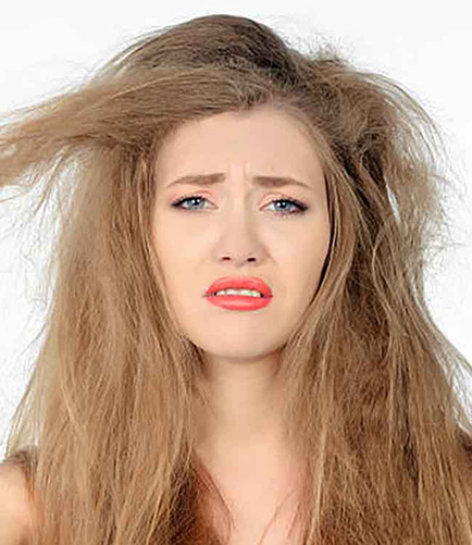 Woman with brown open hair holding rough strands and frowning — representing damaged, brittle, and unhealthy hair