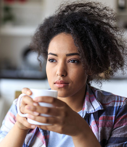 Woman with curly hair in a T-shirt holding tea, pausing in thought — symbolizing hormonal imbalance and the need for inner balance