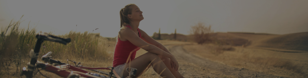 About Us banner showing an athlete seated on the desert surface with a bicycle nearby, reflecting Brit Finds’ journey of resilience, nature, and wellness on desktop