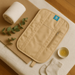 Flat lay of waist wrap placed on a towel with a small bowl of oil and green leaves beside it — showing natural castor oil ritual setup