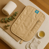 Flat lay of waist wrap placed on a towel with a small bowl of oil and green leaves beside it — showing natural castor oil ritual setup