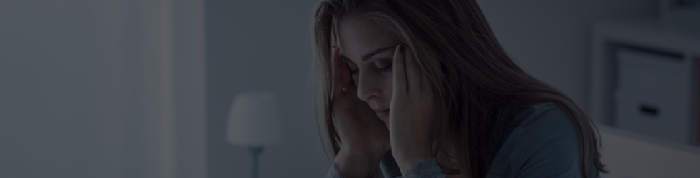 Woman with open hair sitting and holding her forehead with both hands — representing emotional stress and sleep disturbance for desktop view
