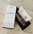 Open box display of 200ml castor oil bottle placed on a marble table, with the bottle slightly pulled out of the box and a thank-you card resting on top, showcasing premium packaging and natural wellness presentation.